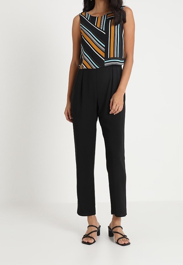 Femme portant un haut sans manches à rayures multicolores, un pantalon noir taille haute à jambes droites et des sandales noires à talons blocs avec brides.