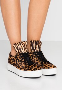 Sneaker con stampa leopardata e texture pelosa, lacci neri e suola in gomma bianca. Il design con risvolto alla caviglia aggiunge un dettaglio distintivo.