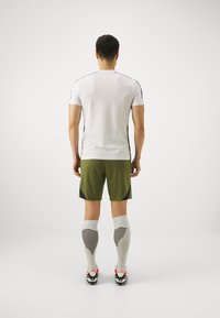 Vit atletisk t-shirt med svarta sidosstreck, gröna shorts med texturerad design, vita strumpor med svarta ränder och röda skor med accenter.