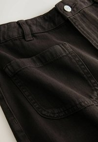 Gros plan sur un tissu en denim noir montrant une poche arrière, une passants de ceinture et un bouton en métal sur un pantalon.