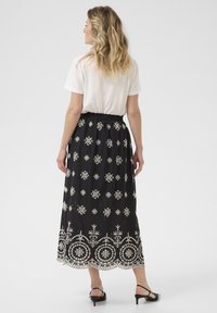 Zwarte maxi rok met witte geborduurde bloemenpatronen, met een geraffineerde taille en een gegolfde kantzoom. Gemonteerd met een wit T-shirt.
