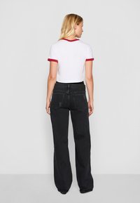 White cropped t-shirt with red trim, paired with high-waist black wide-leg jeans featuring back pockets and subtle distressing.