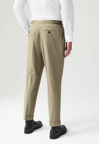 Pantaloni bej cu dungi subțiri, cu o croială ajustată, având două buzunare la spate, bucle pentru curea și manșete răsucite. Asortați cu pantofi negri.