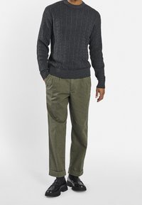 Tummanharmaa cable-knit-neulepaita yhdistettynä oliivinvihreisiin laskostettuihin housuihin, joissa on käännetyt hihansuut ja mustat loafers-kengät.