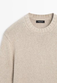 Béžový pletený svetr s žebrovaným kulatým výstřihem a viditelnou značkou Massimo Dutti na zadní straně límce.