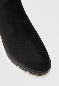 Melnas zamšādas potīšu zābaki ar smailu purngalu, izšūtu detaļu un gumijas zoli ar rievotu rakstu, kas nodrošina saķeri.