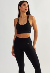 Czarny stanik sportowy z cienkimi ramiączkami i prążkowaną fakturą, w połączeniu z czarnymi legginsami o wysokim stanie z małym logo serca.