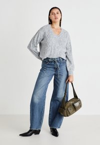 Pull en maille grise avec un col en V, manches amples ; jeans blue wide-leg taille haute ; bottines noires à talons pointus ; sac à main vert olive.