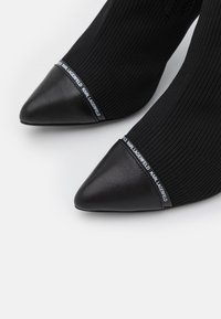 Bottes chevilles noires de style chaussette avec des pointes en cuir, un tissu ribbé et un accent de marque en haut de la tige.