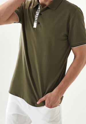 Polo shirt verde oliva realizzato in tessuto texture, con colletto classico, pattina con bottoni e dettaglio logo bianco sul colletto.