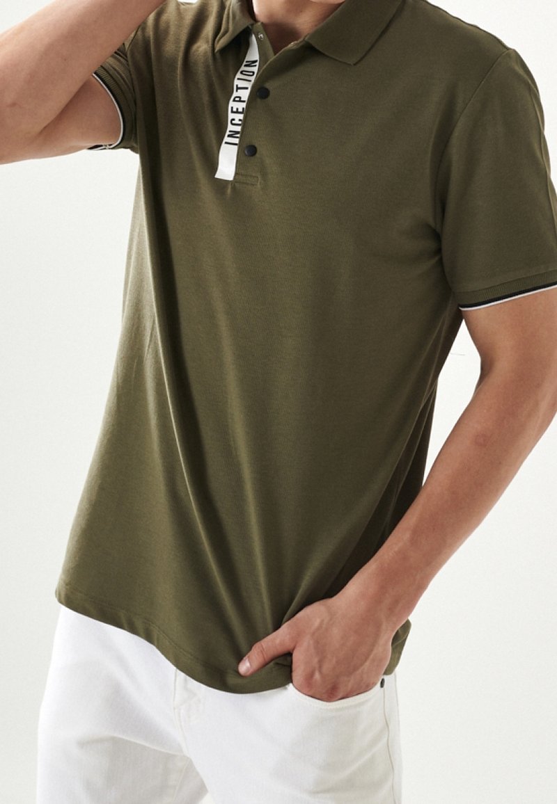 Polo shirt verde oliva realizzato in tessuto texture, con colletto classico, pattina con bottoni e dettaglio logo bianco sul colletto.