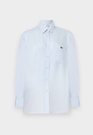 Svetlo modra srajca z dolgimi rokavi, gumbki, s prsnim žepom in majhnim zelenim logotipom krokodila na žepu.