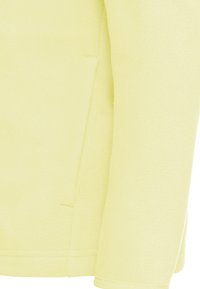 Κοντινό πλάνο σε ανοιχτό κίτρινο ύφασμα φλις με κάθετη σχισμή τσέπης και ραφές στο μανίκι και στο πλάι.