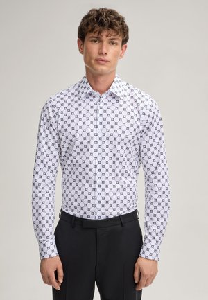 Camicia bianca con un motivo geometrico ripetuto in navy, colletto a punta, chiusura con bottoni e maniche lunghe, abbinata a pantaloni neri.