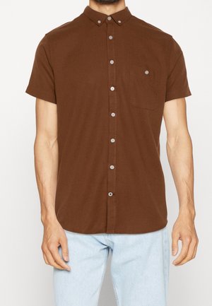 Camisa de botones de manga corta en color marrón con cuello, bolsillo en el pecho y botones de color claro. La tela tiene una textura suave.