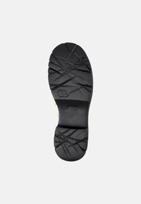 Suola di scarpa in gomma nera con un motivo testurizzato e design a incrocio per una migliore aderenza, caratterizzata da un bordo liscio e un insignia del logo vicino al centro.