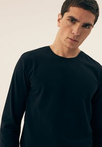 Schwarzes Langarmshirt aus glattem Baumwollstoff, mit einem runden Halsausschnitt und einer taillierten Passform. Minimalistischer Stil ohne sichtbare Muster.