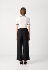 Witte geribde polo met zwarte accenten, gecombineerd met een ontspannen zwarte broek met achterzakken. Zwarte schoenen maken de outfit compleet.