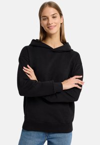 Schwarzer Hoodie mit einer frontalen Kängurutasche und verstellbarem Kapuzenzug. Der Stoff wirkt weich, mit gerippten Bündchen und Saum. Getragen mit hellblauen Jeans.