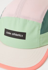 Colorful cap with pink, green, and cream sections. Made of textured fabric, featuring a black logo label. Visor has a pink accent.