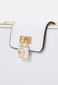 Sac à main synthétique blanc avec fermeture à serrure en ton doré, coutures élégantes et bordures contrastantes noires le long des bords.