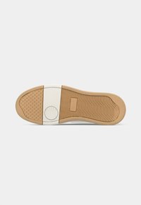 Shoe sole with beige rubber and white stripe, textured tread patterns, and a circular grip detail near the heel area.