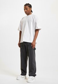 Camiseta blanca de algodón suelta combinada con pantalones cargo gris oscuro con bolsillos laterales, complementada con zapatillas blancas gruesas.