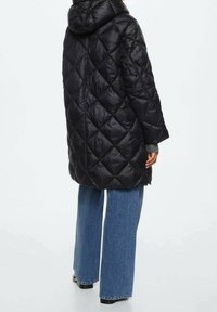 Sort dunjakke med hætte, med et diamant-quiltet mønster, løs pasform og knælængde, kombineret med vide blå jeans.