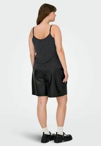 Top sin mangas negro con patrón y tirantes finos, combinado con pantalones cortos de piel sintética negra a la altura de la rodilla. Zapatos negros de suela gruesa y calcetines blancos visibles.