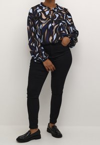Sort langærmet bluse med abstrakte blå og brune svajer, flæset halsudskæring og snørebånd. Kombineret med sorte skinny jeans og shiny loafers.