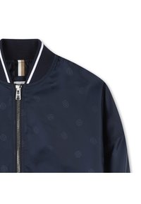 Veste de pilote marine avec fermeture éclair, col côtelé et motif de logo subtil sur un tissu lisse. Accents rayés contrastés près du cou.
