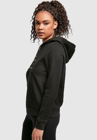 Sweatshirt à capuche noir avec une poche avant, présentant une capuche à cordon de serrage et un tissu doux et texturé. Design simple adapté à un usage décontracté.