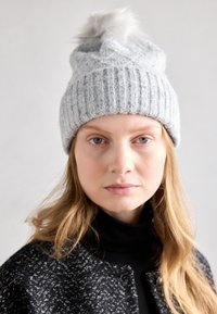 Berretto grigio lavorato a maglia con texture a coste, caratterizzato da un pompon in pelliccia sintetica sulla sommità. Contiene piccole perline decorative per un tocco di stile in più.