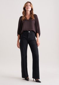 Jeans grigio scuro a vita alta con gamba dritta, abbinati a una blusa marrone scuro con scollatura a V e maniche a palloncino. Tacchi neri a punta completano il look.
