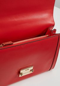 Rød læderhåndtaske med en guldtonet hardwarelukning og en intern lynlåslomme til sikker opbevaring.