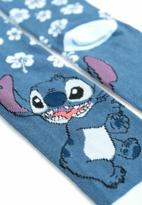 Calzini blu con un personaggio dei cartoni animati con orecchie viola, pancia bianca e un'espressione giocosa, decorati con motivi floreali bianchi.