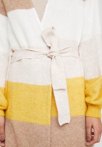 Sweter kardigan w beżowe, białe i żółte paski. Posiada fason kopertowy, pasek do przewiązania oraz miękką, teksturowaną przędzę.