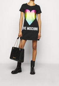 Czarna sukienka t-shirtowa z gradientowym sercem w żywych kolorach i białym napisem "LOVE MOSCHINO". Do kompletu czarna pikowana torebka i czarne botki.