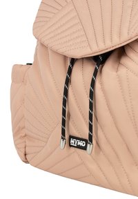 Quilted beige rygsæk med en blød tekstur, der har sorte snore, sølvfarvet hardware og et logo-patch på siden.