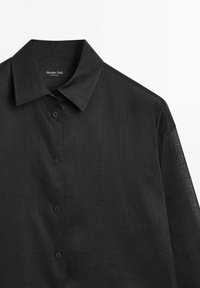 Camicia nera con bottone in un tessuto leggero, dotata di un colletto classico e una texture sobria, con bottoni neri e un design dalla vestibilità ampia.