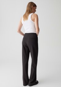 Pantaloni neri sartoriali con gamba dritta e tasche posteriori sottili, indossati con un top bianco senza maniche, che mette in mostra un design pulito.