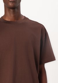 Braunes Baumwoll-T-Shirt mit Rundhalsausschnitt, kurzen Ärmeln und lockerer Passform, mit glatter Textur und ohne sichtbare Muster oder Verzierungen.