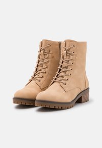 Brązowe botki sięgające kostki wykonane z zamszu, z okrągłym noskiem, sznurowanym przodem i zamkiem błyskawicznym z boku. Posiadają Solidną gumową podeszwę i słupek.