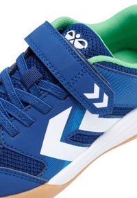 Chaussure de sport bleue avec une tige en maille et en synthétique, mettant en valeur des accents blancs et verts, une sangle Velcro et une semelle en caoutchouc texturé.