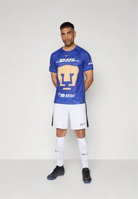 Modra nogometna majica z zlatim levjim logotipom in napisom "DHL", kombinirana z belimi kratkimi hlačami in črnimi nogometnimi čevlji. Obleko dopolnjujejo bele nogavice.