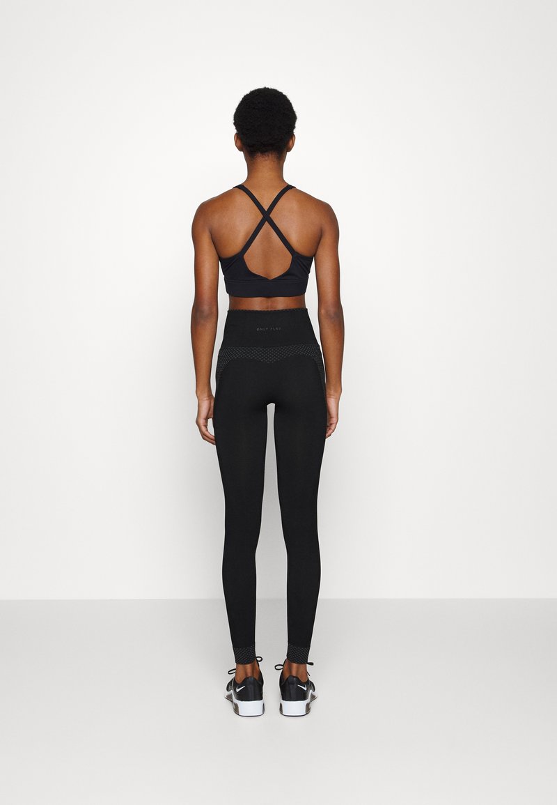 Czarny stanik sportowy z krzyżującym się tyłem, w połączeniu z czarnymi legginsami o wysokim stanie z teksturowanymi akcentami. Czarne buty sportowe.
