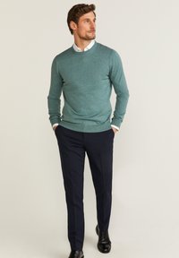 Mörkblå-grön stickad tröja för män med rund halslinning, kombinerad med mörkblå byxor och svarta skor, med en slät yta.