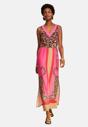 Frau trägt ärmelloses pinkfarbenes Maxikleid mit Leopardenoberteil und zwei großen Leopardenabbildungen auf dem Rock, geht nach vorne.