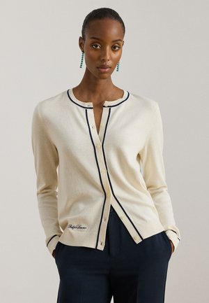 Kremowy kardigan wykonany z miękkiej tkaniny, z ciemnoniebieskimi lamówkami, zapięciem na guziki oraz haftowanym logo marki przy krawędzi.