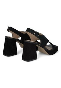 Sandales ouvertes en suede noir avec un design à large bandage, boucle ajustable à la cheville et talons carrés épais. Texture lisse et construction robuste.